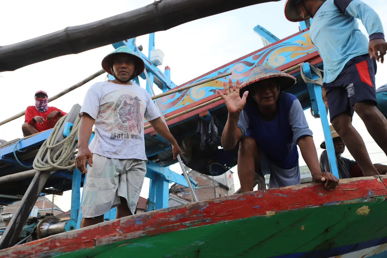 Nelayan tersenyum dan melambai dari atas perahu kayu berwarna-warni